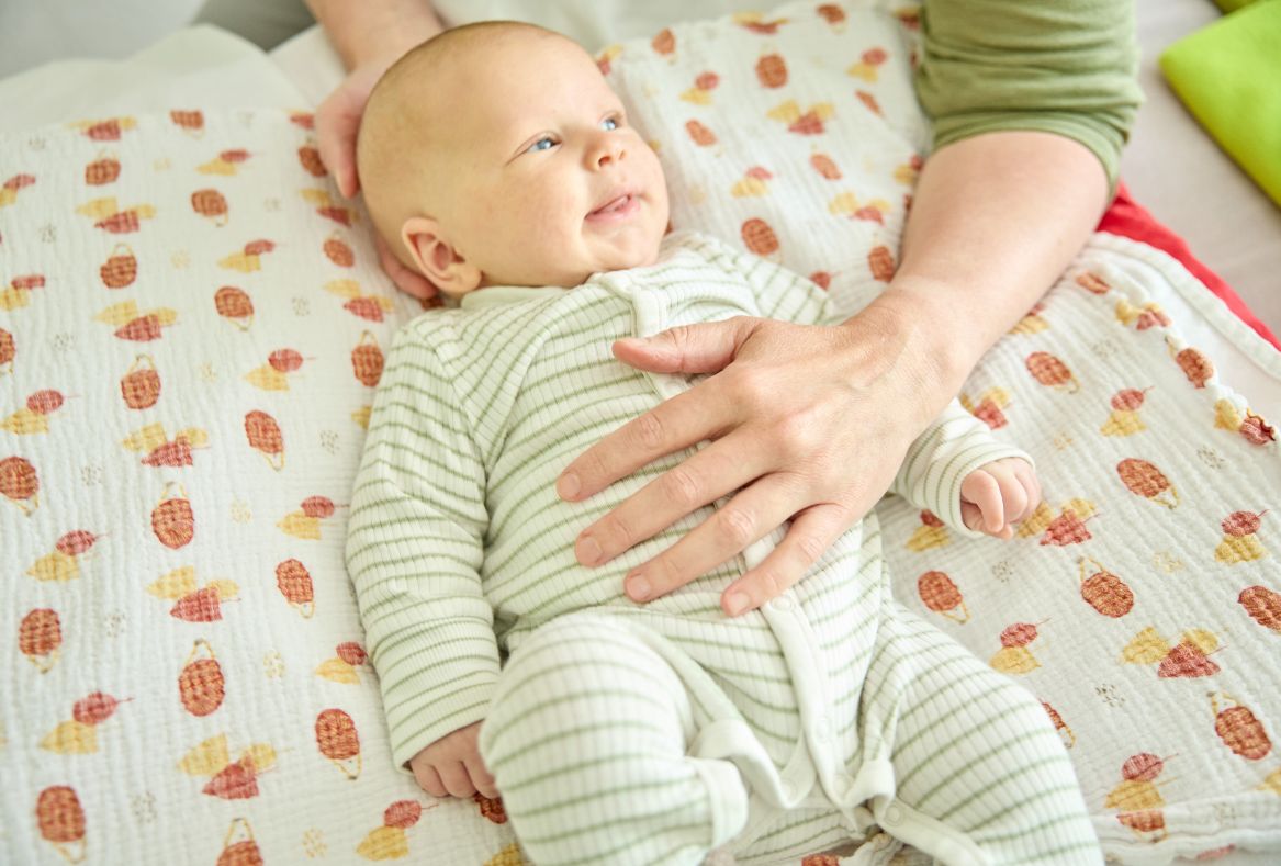 Baby auf einer Matte, Hand der Osteopathin auf dem Bauch