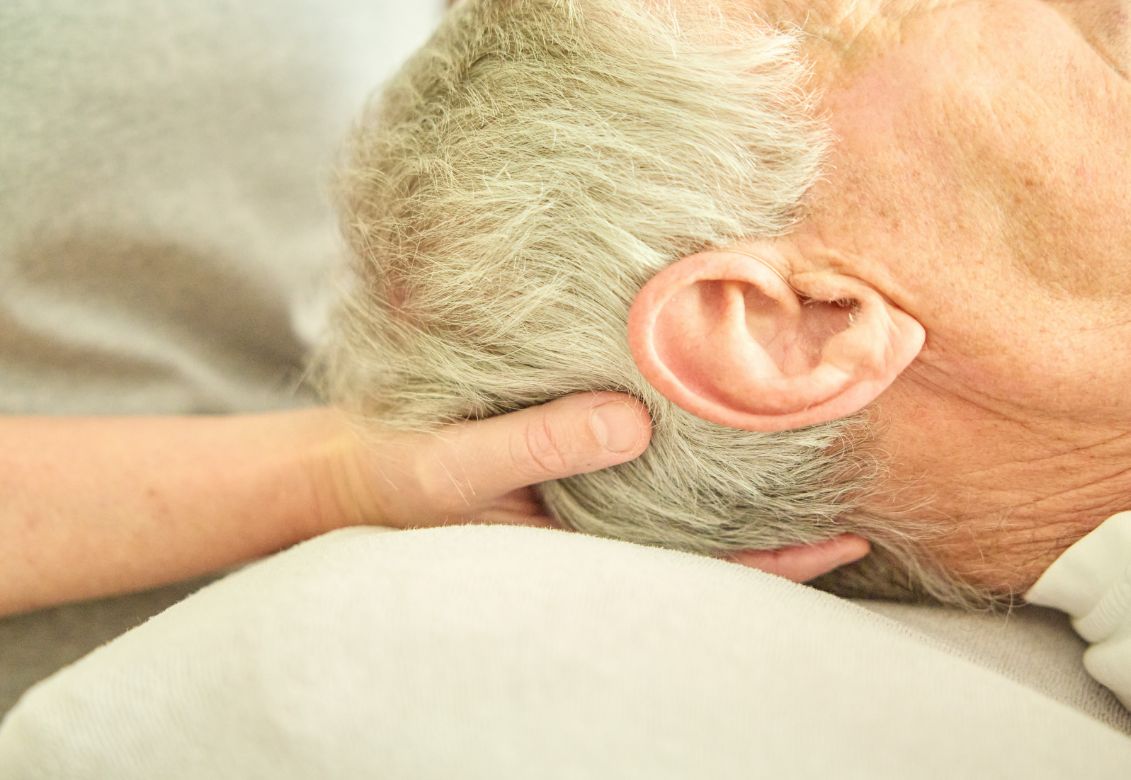 Hände der Osteopathin am Nacken eines Patienten
