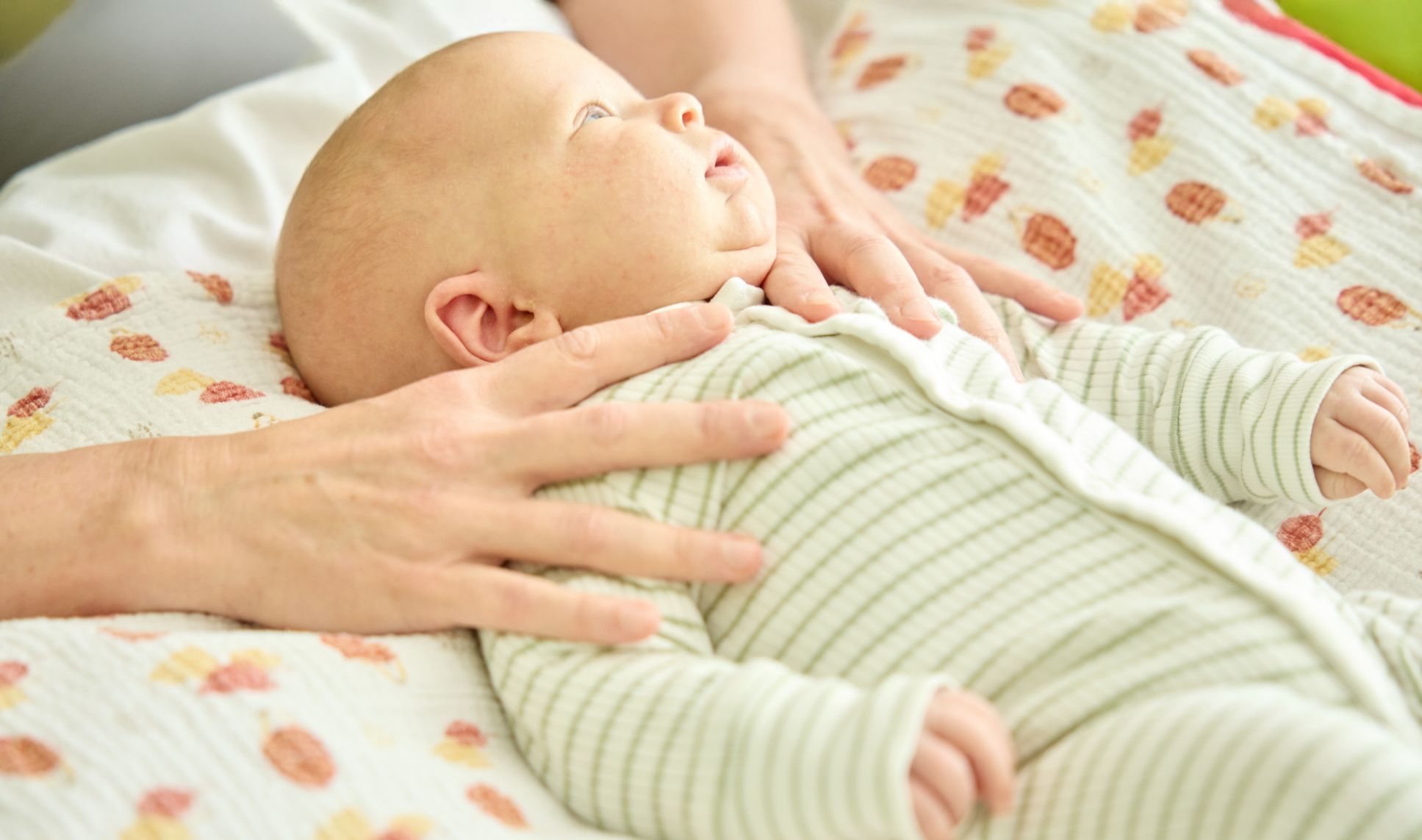 Säugling im Strampelanzug, liegend, Hände bei osteopathischer Behandlung
