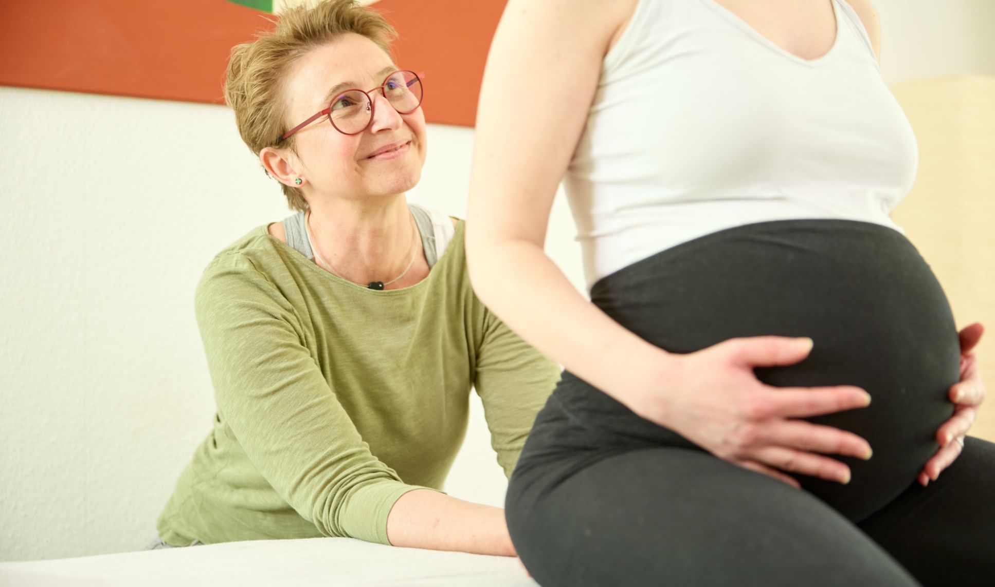 Schwangere Frau, nur Bauch und Brust zu sehen, Hände auf dem Bauch, Meike Fritzen dahinter stehend